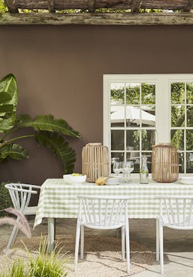 Outside dining table and chairs with the back wall painted in rich chocolate shade 'Scullery' with white panelled doors and a large plant.