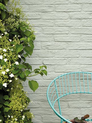 Exterior brick wall painted in grey-green 'Normandy Grey' with a bush to the left and a Turquoise Blue chair to the right.