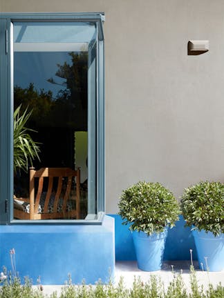 House exterior with a large window, walls painted in neutral grey (Slit) and bright blue (Tivoli), and matching plant pots.