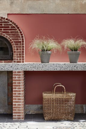 Outdoor kitchen painted in deep terracotta red 'Tuscan Red' with brickwork, plants and a basket.