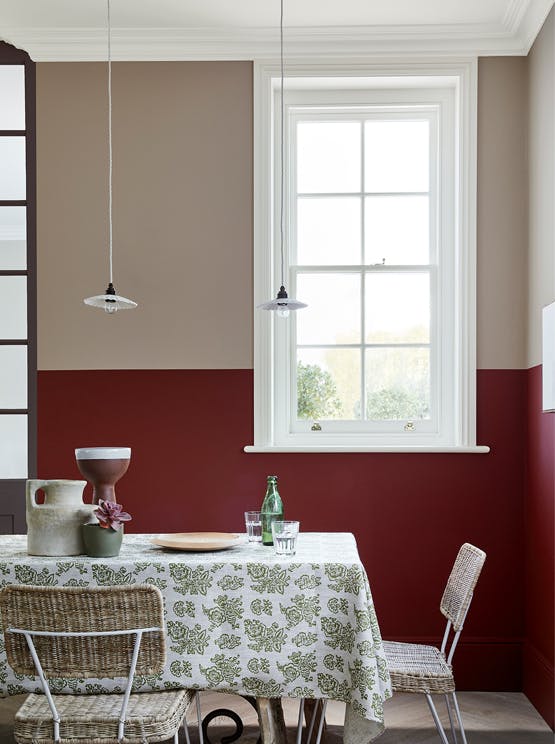 Dining room with upper wall in warm neutral 'Rolling Fog - Dark' and lower wall in deep red 'Arras', with a table and chairs.