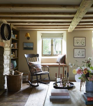 Living room with a low ceiling with beams, brick wall to the left and a blue sofa to the right topped with checked cushions.