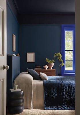 Bedroom painted in rich blue shade 'Royal Navy' with a bright blue 'Smalt' window frame, dark blue on the ceiling and a bed under the window.