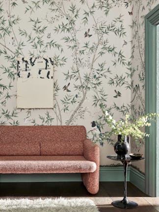 Living room with an off-white bird print mural wallpaper (Belton Scenic - Oyster) with a pink sofa and small table.