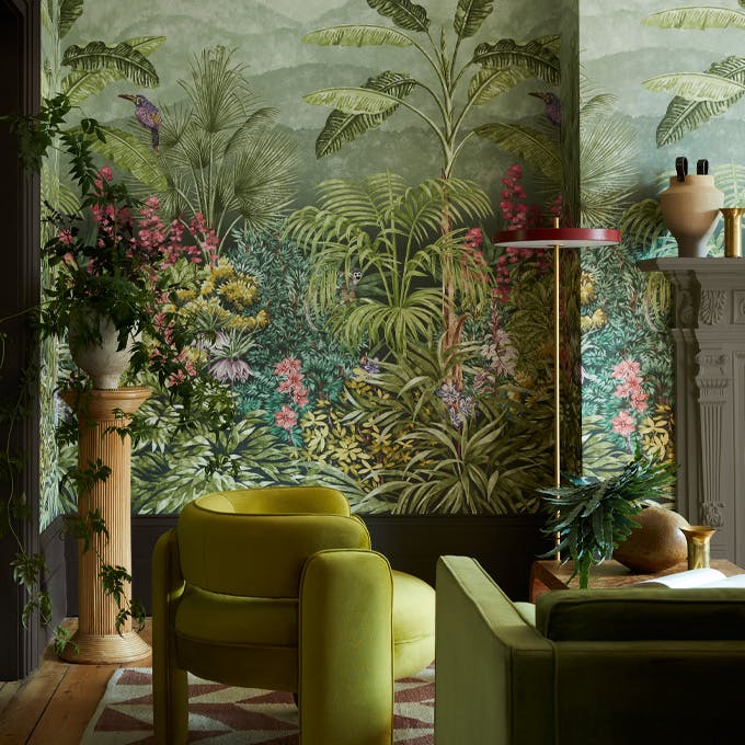 Living space featuring green tropical mural wallpaper (Capricorn - Boringdon) with a green armchair and sofa next to a fireplace.