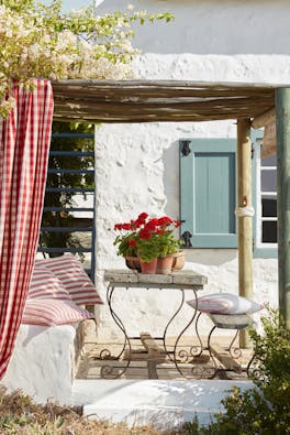 Yard with exerior wall in off white Wood Ash and pale blue shutters (Celestial Blue) with a seating area surrounded by trees.