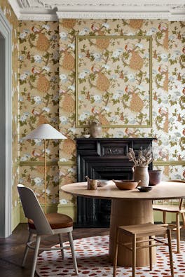 Dining room with metallic bird print wallpaper (Pavona - Gina) and a wooden dining table and chairs in front of a fireplace.