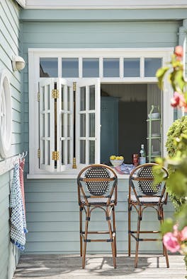 Outside breakfast bar with cladded walls painted in grey blue shade 'Celestial Blue' with two wooden stools under white shutters.