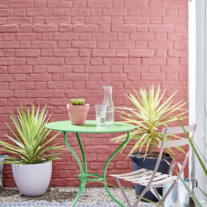 Outside brick wall painted in red shade 'Ashes of Roses' with bright green garden table and pink chair.