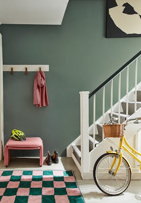 Grey green (Livid) painted hallway with grey carpeted stairs leading to a checkered rug and yellow bicycle. 