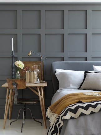 Paneled bedroom painted in dark grey 'Scree' with a small wooden desk next to a grey bed on a white floor.