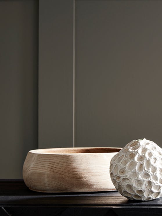 Close-up of wall paneling in a neutral brown shade (Rolling Fog) behind a wooden bowl and stone-colored ornament.