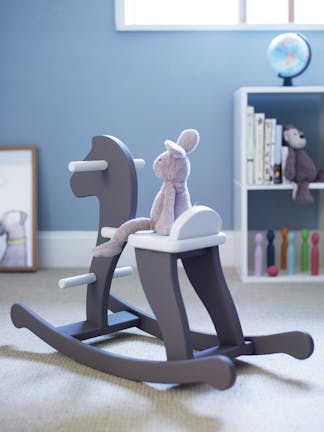 A blue nursery with powder blue (James) walls featuring a bookshelf and a brown rocking horse with a soft toy on top.