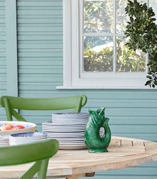 Close-up of a light blue shed behind a wooden table and green chairs.