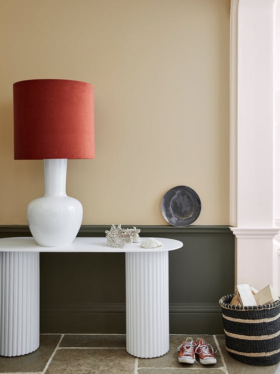 Pale brown neutral hallway (Lute) with lower wall painted in grey green (Pomeranian Ash) and a white side table and large lamp.