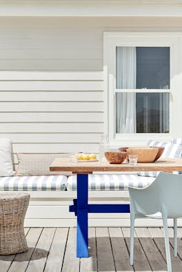 Outdoor dining area with off white paneled wall (Linen Wash) with a striped cushioned chair and wooden table.