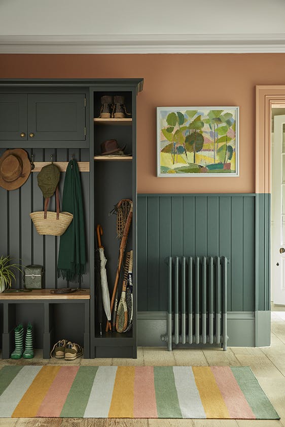 Paneled boot room with the top half painted in 'Split Pink' and the lower wall in 'Harley Green' with a cupboard to the left and a multi-colored stripy rug.
