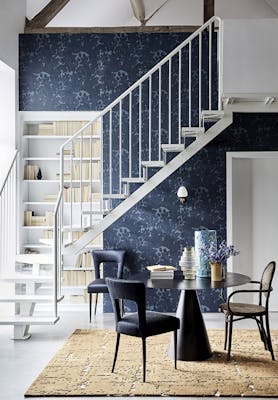 Hallway with dark blue damask wallpaper (Tulip - Blue Black), a black table and chairs, and white stairs passing a bookcase.