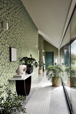 Long hallway with two tone blue and green wallpaper (Beech Nut - Florence) with a big window and plants.