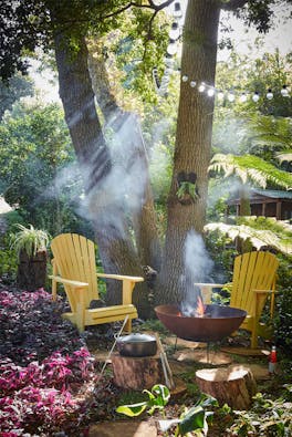 Forest with two bright yellow garden chairs (Giallo) with a barbeque lit surrounded by trees.