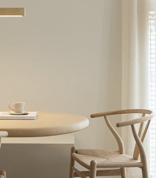 Neutral off-white Portland Stone walls in a dining room with light wooden table and chairs and white translucent curtains.