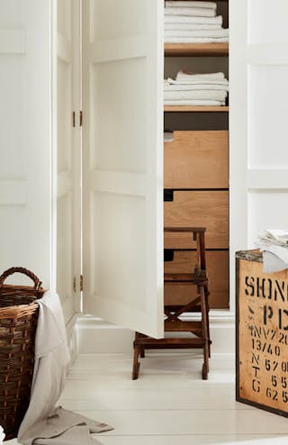 Laundry room color drenched in off white 'Linen Wash' with the closet door opened showing wooden drawers and folded laundry.