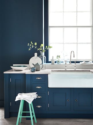 Kitchen painted in dark blue (Hicks' Blue) with a contrasting bright green (Green Verditer) stool underneath a window.