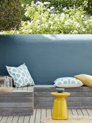 Outside seating area with an Air Force Blue back wall and a wooden panelled bench with cushions.