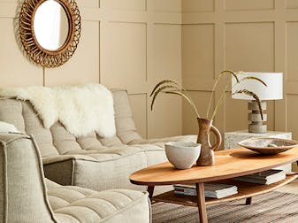 Paneled living space painted in warm neutral 'Travertine' with two sofas and a wooden coffee table.