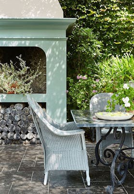 Outside dining area with Aquamarine - Deep fireplace, dining room table and wicker chairs surrounded by trees and plants.