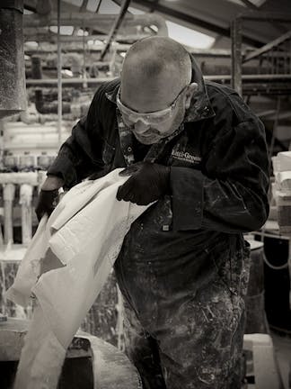 Man in factory wearing safety goggles and a jumpsuit, pouring powder into a container to manufacture Little Greene paints.