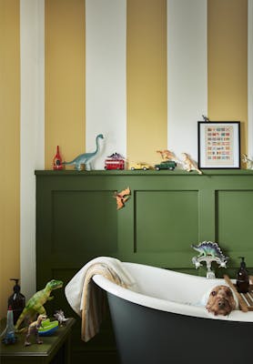 Yellow (Yellow-Pink) and white (Silent White) striped bathroom walls with deep green (Hopper) panelling and bathtub with a dog sat inside.