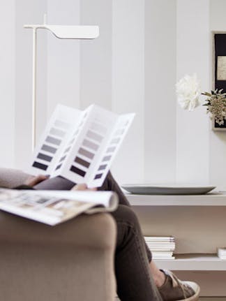 A woman sitting on a sofa next to a stripy wall whilst looking through a Little Greene Color Card.