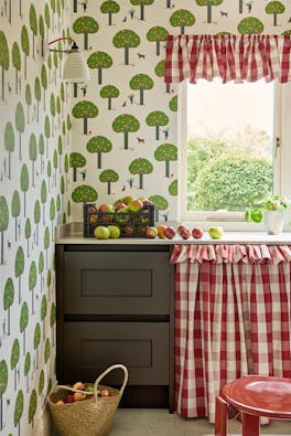 Pantry featuring tree print wallpaper (Rodney Street - Sage & Onions) with dark brown drawers and red gingham hideaway curtain under a window.