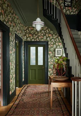 High ceiling hallway featuring dark green floral wallpaper (Aderyn - Olive Colour) with dark green woodwork and a tapestry rug.