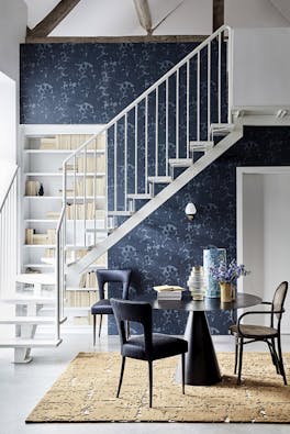 Hallway with dark blue damask wallpaper (Tulip - Blue Black), a black table and chairs, and white stairs passing a bookcase.