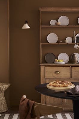 Dining space painted in orange-brown shade 'Galette' with a wooden dining table and a large wooden dresser and plates.