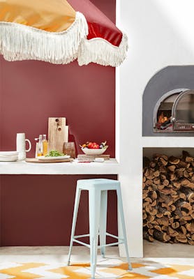 Outside dining area with deep red walls (Arras), a pizza oven, counter and a parasol umbrella.