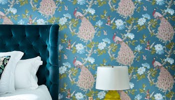 Bedroom with a blue bird print wallpaper (Pavona - Silvie) and a small wooden table next to the bed.