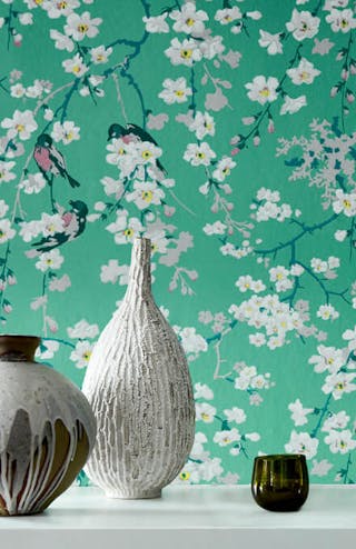 Close-up of green printed floral and bird wallpaper (Massingberd Blossom - Verditer), with two ornaments in front.