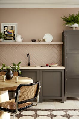 Kitchen painted in muted pink shade 'Mochi' with contrasting neutral brown 'Attic II' units with a dining room table and chair.