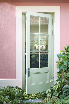 Exterior door painted in light green (Salix) with contrasting pale pink (Hellebore) wall surrouneded by plants.