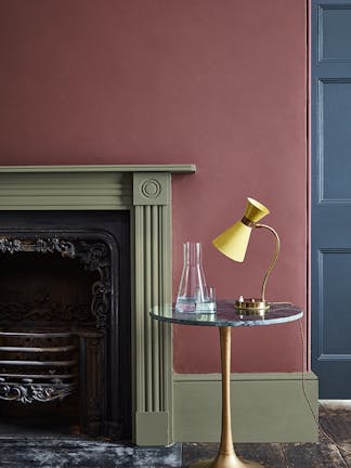 Living room wall painted in plum purple shade 'Adventurer' with a sage green fireplace and a wooden floor.