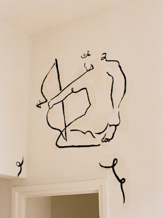 Painted dark outline of a human using a crossbow featured on a white interior wall above a door frame.