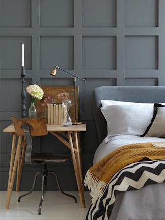 Paneled bedroom painted in dark grey 'Scree' with a small wooden desk next to a grey bed on a white floor.