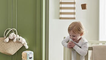 Calm nursery space with a green (Green Stone - Pale) wardrobe on the left and a crib on the right with a side table and fluffy toys on the floor.