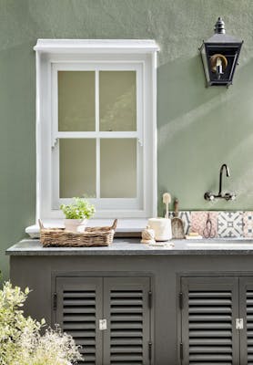 Outside kitchen sink area in grey green 'Boringdon Green' with a contrasting grey cabinet and white window frame.