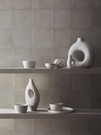 Close-up of a wall comprised of light grey square tiles painted in 'French Grey' with shelves holding light grey ornaments.