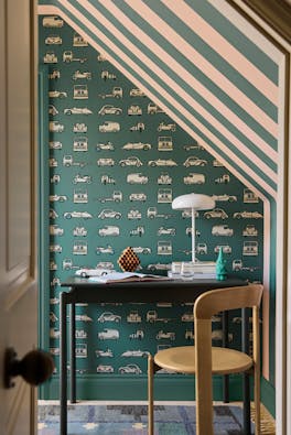 Home office space featuring car print wallpaper (Road Trip - Pleat) on the back wall and striped wallpaper on the right (Broad Stripe - Pleat) with a desk and chair.