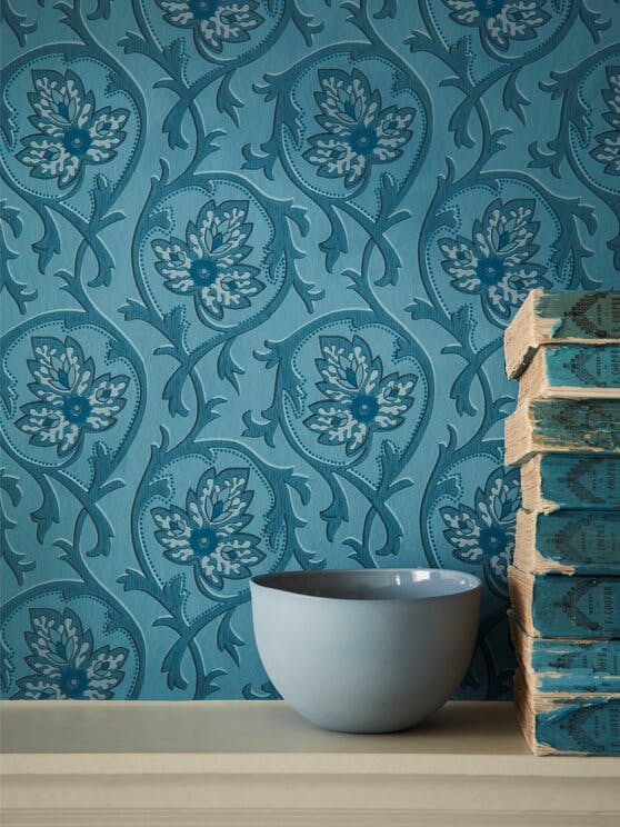 Close-up of National Trust tonal blue wallpaper behind a grey-blue bowl and eight books stacked on top of each other. 